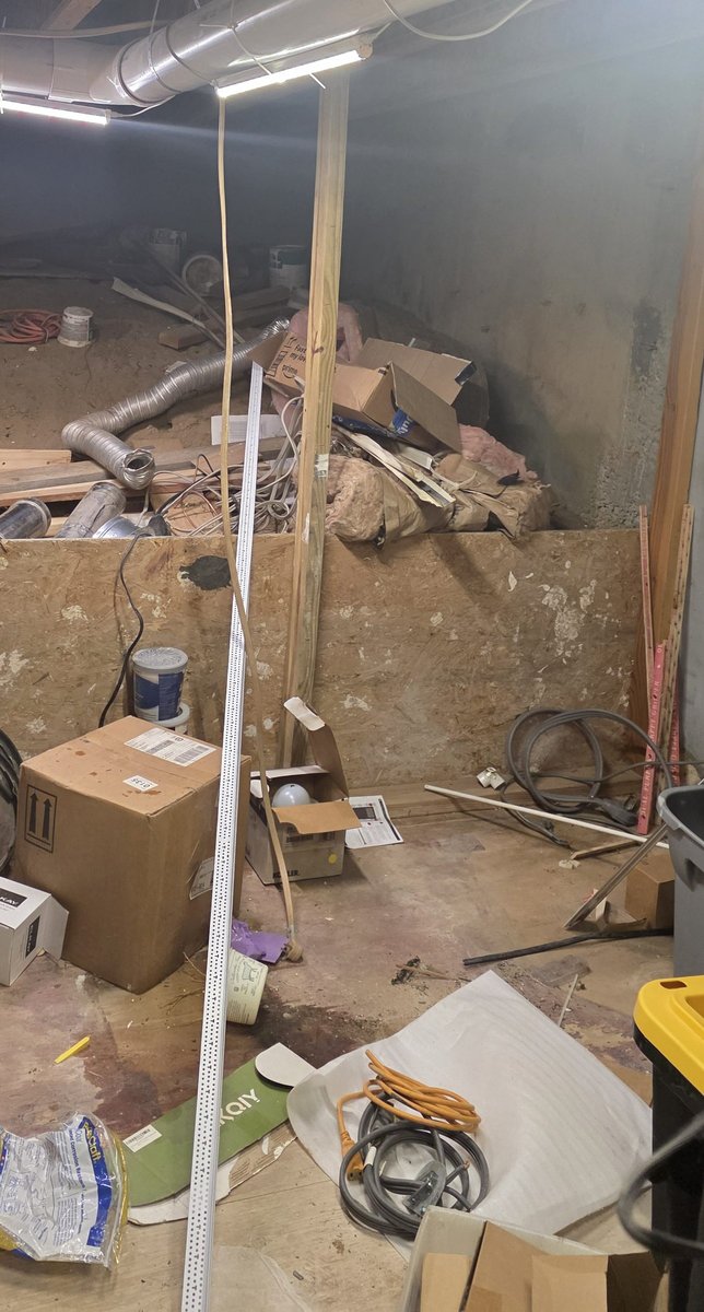 Before: unfinished basement with boxes, ducting, hoses, cables and debris across the floor